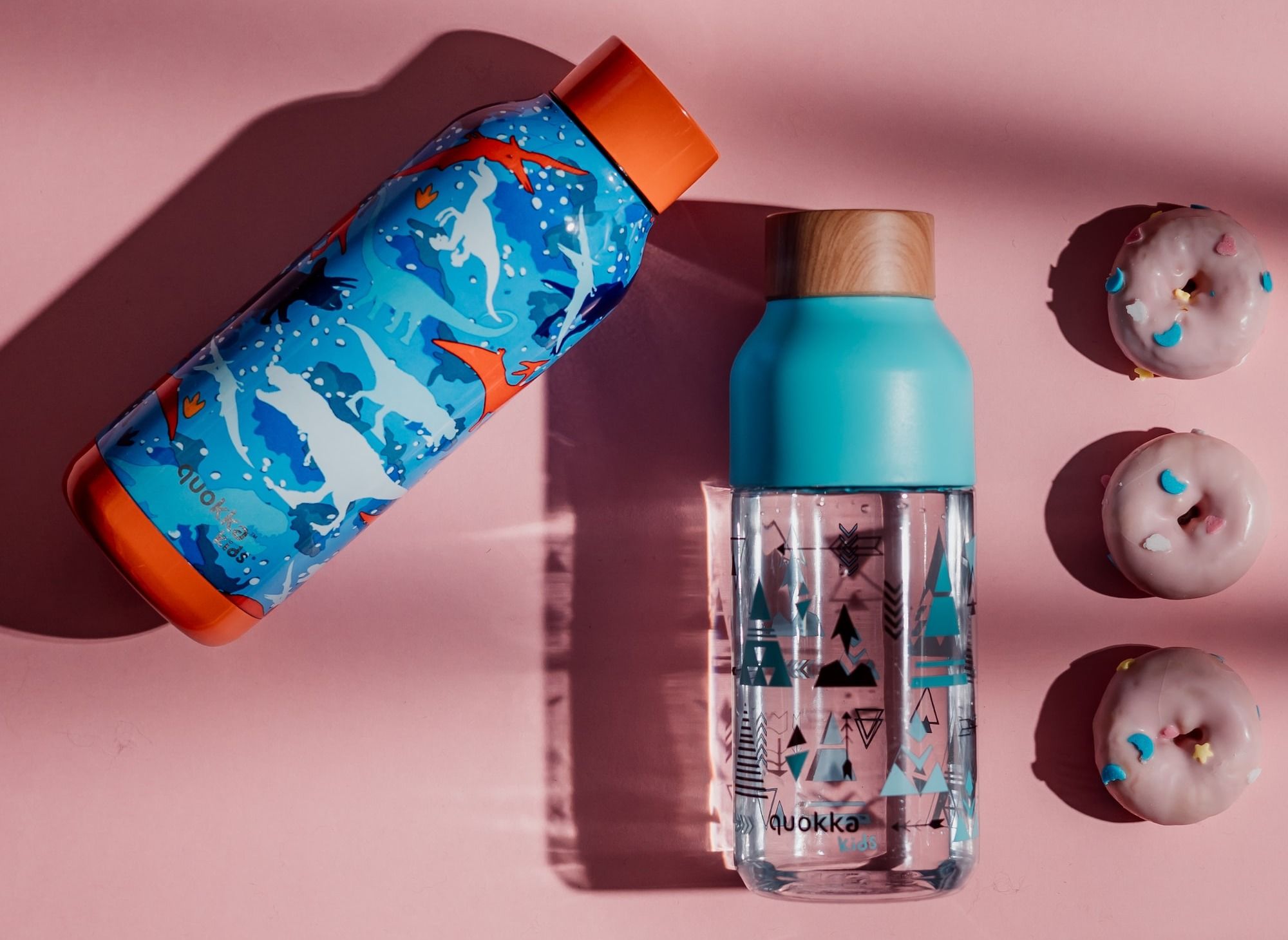 a bottle of water next to three donuts on a pink surface